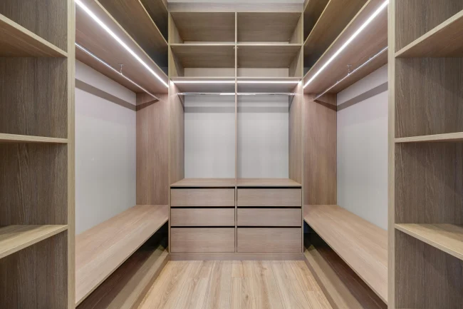 A luxurious walk-in wardrobe featuring modern custom closet systems with built-in drawers, shoe organizers, adjustable wood shelving, and upscale custom lighting.